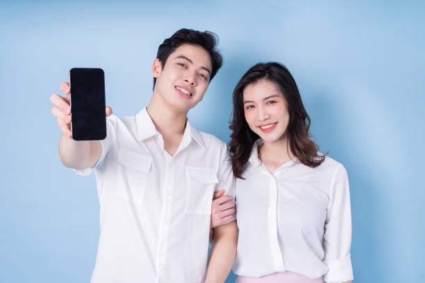 istock Image of young Asian couple using smartphone on blue background 1390002573