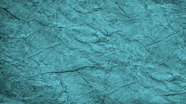 Photo of Dirty turquoise grunge background. Toned rough cracked rock surface texture. Close-up. Stone background with space for design.