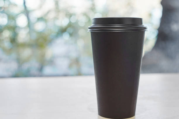 istock Black paper disposable coffee cup standing on a table in a cafe 1390008039