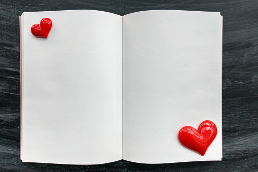 Blank open notebook and red heart on blackboard