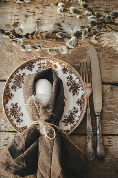 istock Natural egg in napkin with feather, setting  with vintage plate, cutlery, pussy willow branches on aged wooden table. Rustic Easter table setting top view. Easter table decoration 1390014789