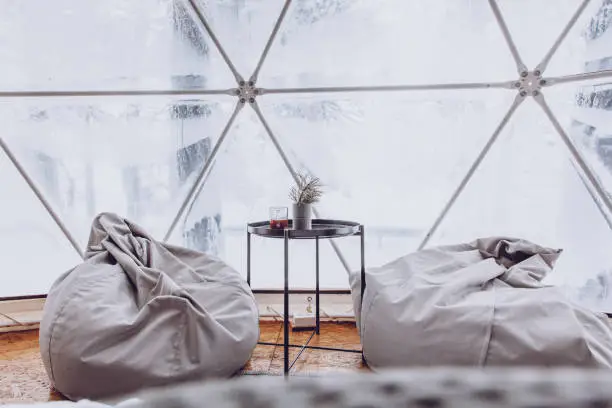 Photo of Two bag chairs and a table with a cup of coffee are in the room of the dome tent with a view of the snow-covered forest.