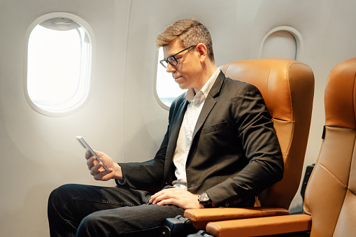 Businessman using smartphone while sitting in airplane, Traveling and technology. Flying at first class.