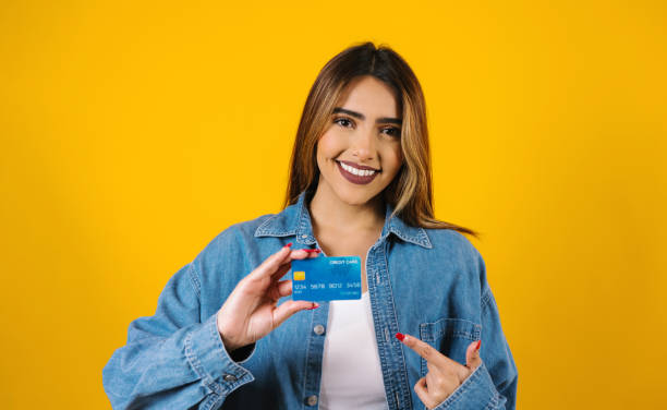 joven latina con tarjeta de crédito para comprar sobre fondo amarillo en méxico américa latina - greeting card holding women credit card fotografías e imágenes de stock