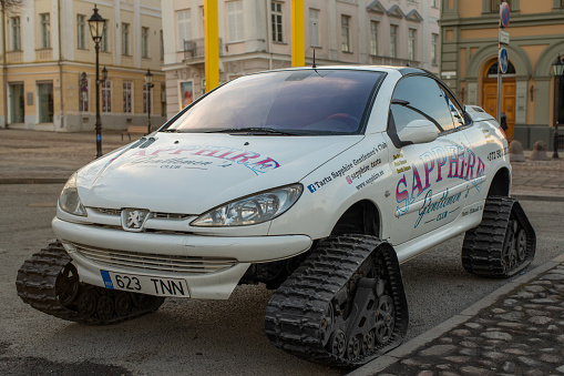 Tartu, Estonia - March 13 2022: Modified white Peugeot 206 2002 parked in Tartu city centre. Caterpillars on a car instead of wheels for driving in the snow.