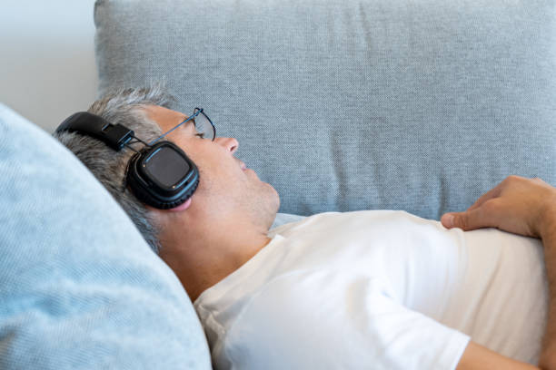 Man lying on sofa sleeping while is listening music with headphones. Relax at home concept stock photo