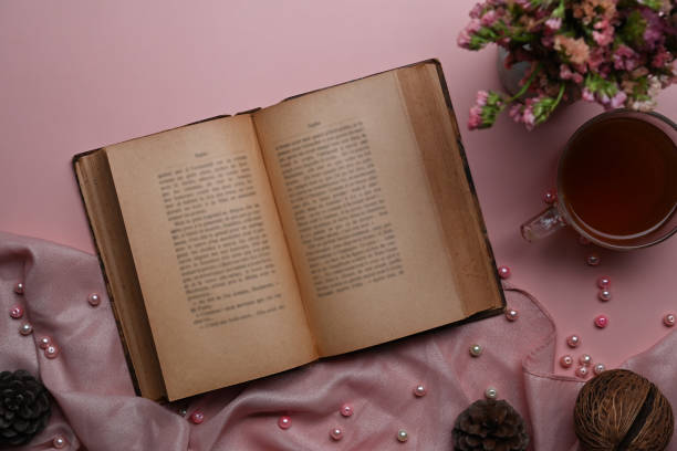 Fla tay with white tulips, pink denim jacket, open vintage book, and cup of tea on pink background - cozy spring morning setup with soft feminine tones.