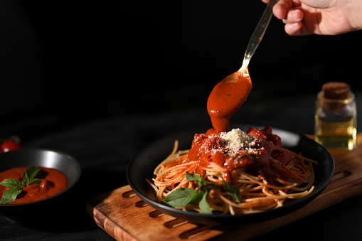 Female hand garnishing and preparing Italian pasta spaghetti with tomato sauce. Italian food concept