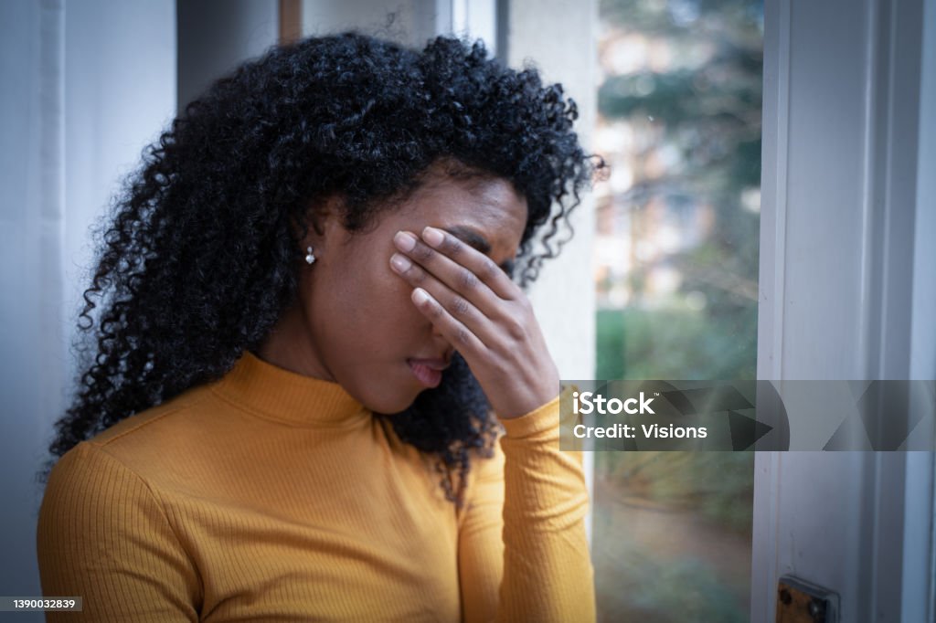 One black woman depressed in front of window A black woman very sad thinking in front of window Black People Stock Photo