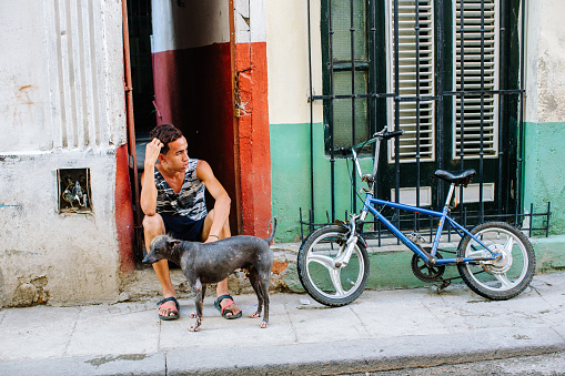 Havana, Cuba - May 2, 2015:  Young cuban boy is waiting somebody with his old dog, in front of his house.