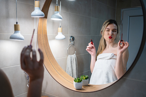 Young Caucasian woman doing her make up in the bathroom, applying the red lipstick