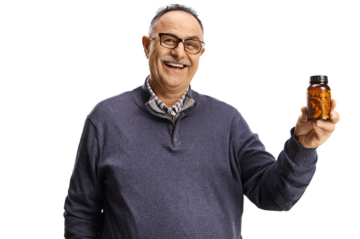 Mature man holding a bottle of medications and smiling isolated on white background