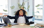 Shot of an adorable little girl dressed as a businessperson sitting alone in an office and throwing money