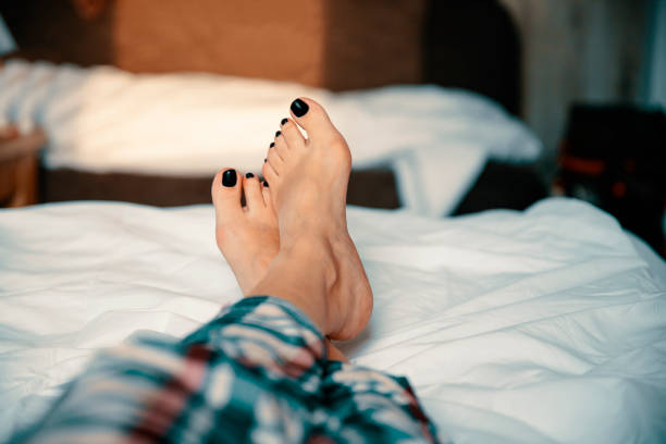 Female relaxing bare foot in bed Woman resting  painful pedicure bare feet in bed. Close up home pedicure stock pictures, royalty-free photos & images