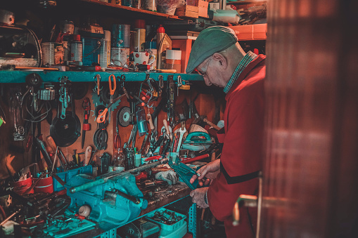 Senior man using a normal wrench and a monkey wrench to tighten the vise and fix a metal piece