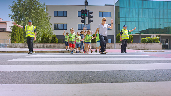 Men crossing guard stop sign while signaling a group of school children to cross the street.