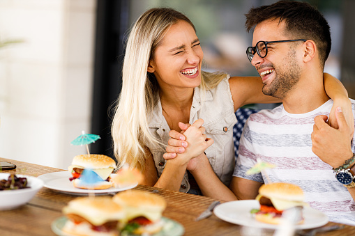 Young cheerful couple enjoying while having a meal at dining table on a patio.