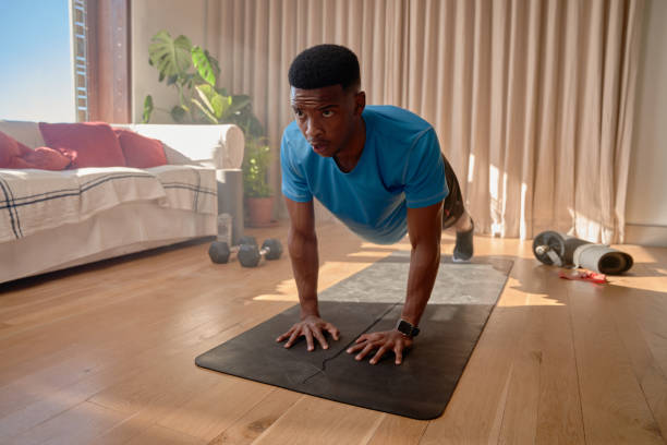 hombre afroamericano sosteniendo tablones altos en la sala de estar, haciendo ejercicio en casa - ewan fotografías e imágenes de stock