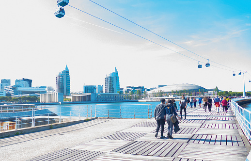 Lisbon, Portugal, 27 April 2019. Tourists walks along the Ribeira das Naus esplanade next to the Tagus river. The esplanade is a popular tourist attraction consisting of shops, restaurants, bars, historical sights, and a cableway.