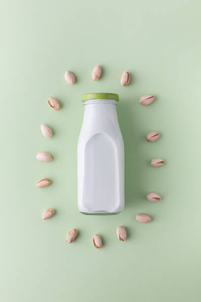 Pistachio milk in the bottle surrounded by pistachios on the green background, top view stock photo