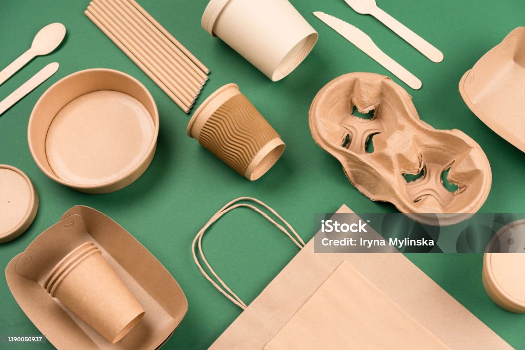 Kraft paper utensils on green background. Paper cups and containers, wooden cutlery. Street food paper packaging, recyclable paperware, zero waste packaging concept. Mockup, flat lay Sustainable Lifestyle Stock Photo