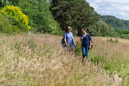 Wide shot of two senior women hiking together in Northumberland in a wilderness area laughing and enjoying the summer. They are walking through long Timothy grass.