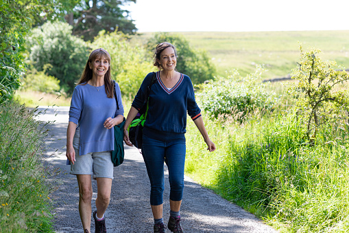 Senior women walking together in Northumberland along a non urban road talking and enjoying the summer.