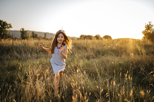 Cheerful girl running in summer nature at sunset