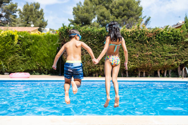 Two funny kid jumping into a swimming pool. Back view.