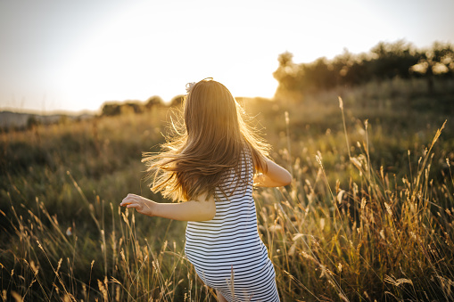 Back view of cheerful girl running in summer nature at sunset