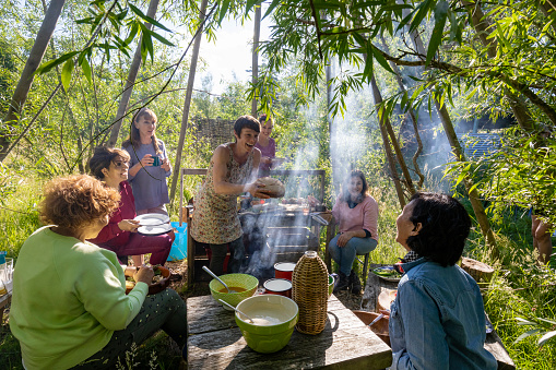 Mature woman teaching a sustainable zero waste cooking class outdoors in Northumberland in a wilderness area. A group of women are watching and participating.