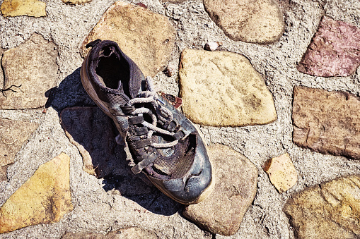 Forlorn damanged running shoe lying abandoned outdoors.