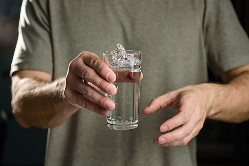 Tremor of the hands when trying to drink. Water splashes from a glass in the hand of a man with tremors, Parkinson's disease.