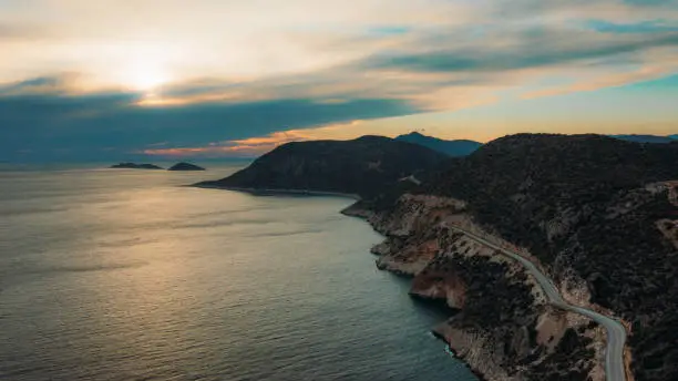 Drone panoramic photo of the highway road surrounded by the sea and the mountains with car driving it during bright dramatic sunset in Antalya Province