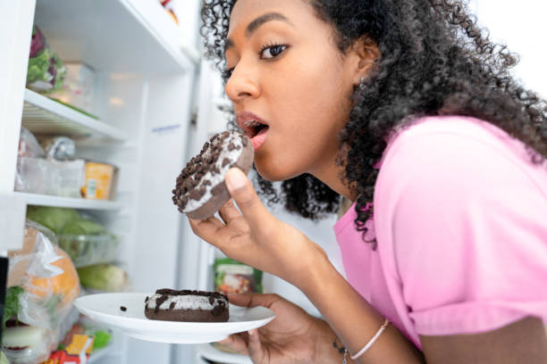 One black woman eating sweeties between meals from the fridge One black woman snacking tempted by sugar sweeties over eating stock pictures, royalty-free photos & images
