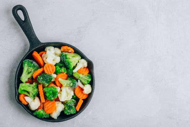 Frozen vegetables. Frozen carrots, broccoli and cauliflower in cast iron pan ready to cook stock photo