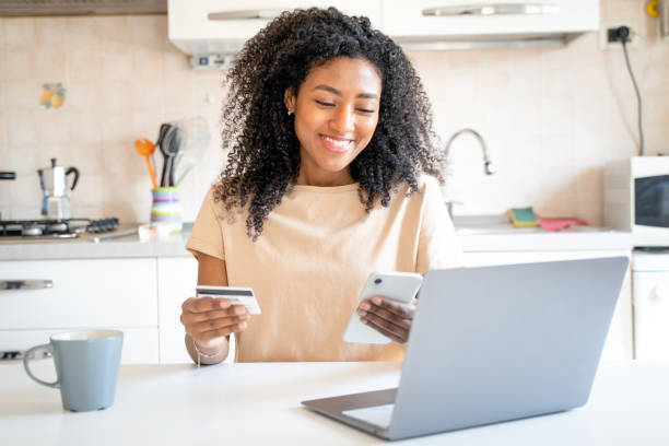 одна счастливая чернокожая женщина совершает покупку кредитной картой из дома - credit card women laptop electronic banking стоковые фото и изображения