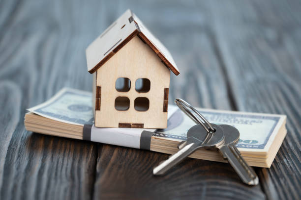 Small toy house with keys on a bundle of banknotes on brown wooden boards stock photo
