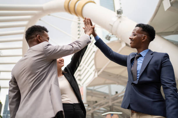 grupo africano e líder caucasiano de pé ao ar livre e dar alta cinco juntos no negócio de sucesso. bom trabalho em equipe e brainstorming para alcançar o resultado das metas corporativas. motivado diverso - sucessor - fotografias e filmes do acervo