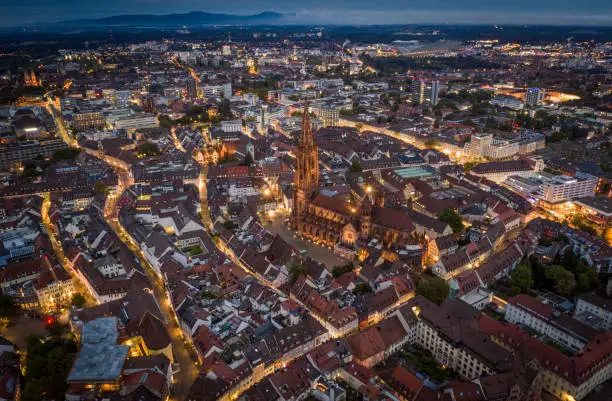 Aerial view of Freiburg im Breisgau. Freiburg Minster (Cathedral) in the center of the frame. Illuminated streets and buildings at dawn. Baden-Wurttemberg in Germany