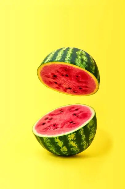 Ripe watermelon cut in half flying in the air on yellow background.