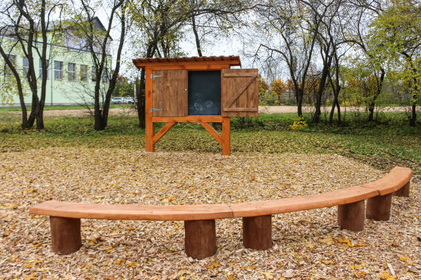 istock Empty outdoor class room with classic chalk board and benches for students with trees as backdrop and brown autumn color leaves on ground. The board can be closed. 1390079010