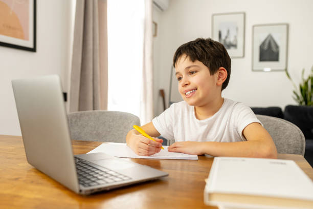 istock Smiling schoolboy studying on the distance from home, using trendy laptop 1390080410