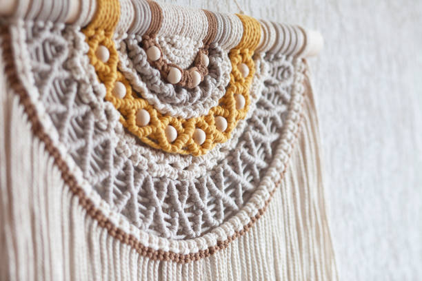 Handmade macrame. 100% cotton wall decoration with wooden stick hanging on a white wall. Macrame braiding and cotton threads. Female hobby. ECO friendly modern knitting  natural decoration in interior stock photo