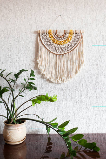 istock Handmade macrame. 100% cotton wall decoration with wooden stick hanging on a white wall. Macrame braiding and cotton threads. Female hobby. ECO friendly modern knitting  natural decoration in interior 1390082983