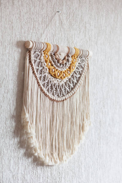 istock Handmade macrame. 100% cotton wall decoration with wooden stick hanging on a white wall. Macrame braiding and cotton threads. Female hobby. ECO friendly modern knitting  natural decoration in interior 1390083005