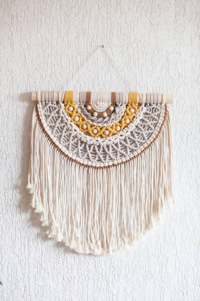 istock Handmade macrame. 100% cotton wall decoration with wooden stick hanging on a white wall. Macrame braiding and cotton threads. Female hobby. ECO friendly modern knitting  natural decoration in interior 1390083013