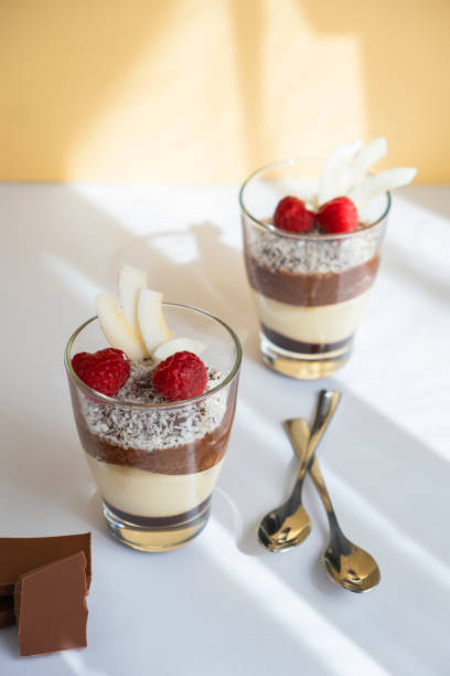 istock Delicious three-layer mousse, vanilla, chocolate, creme brulee dessert in a glass in the bright rays of the sun. Nearby are pieces of milk chocolate 1390085680