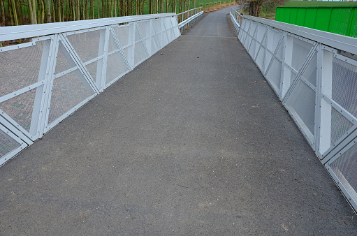 path for cyclists with an asphalt surface. galvanized iron railing over road barriers. Bridge railing with tilting to the sides. railing made of perforated sheet metal in the shape of a triangle, perforated, metal