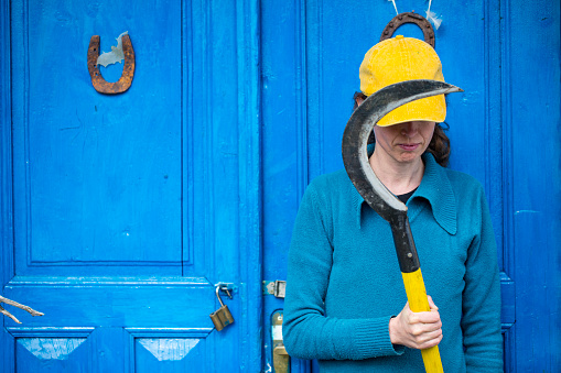 Female Farmer Holding a Sickle In Front of Blue Door.
